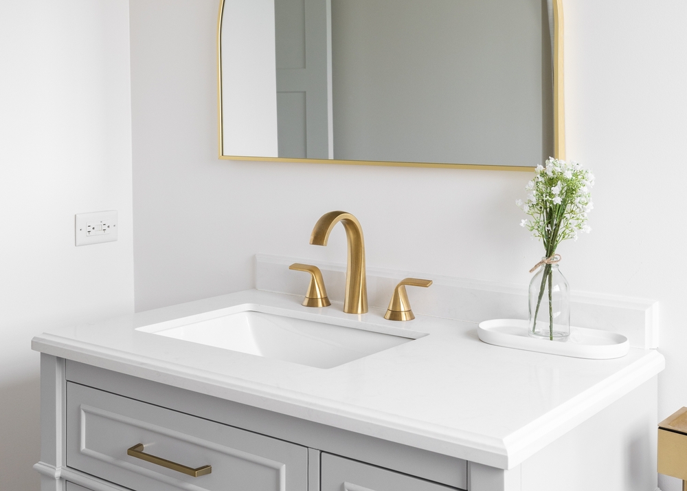 A,gold,bathroom,faucet,detail,with,a,plant,on,the